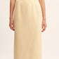 A person wears a sleeveless white top, the POSSE Essie Column Skirt in cream—with a high-rise waist and scalloped hem—and white sandals.