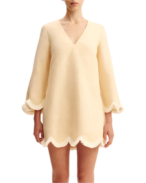 A woman wearing the POSSE Essie Kaftan, a light beige long-sleeve vacation dress featuring a deep v-neckline and scalloped edges on the sleeves and hem.