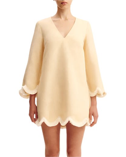 A woman wearing the POSSE Essie Kaftan, a light beige long-sleeve vacation dress featuring a deep v-neckline and scalloped edges on the sleeves and hem.