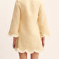 A person is seen from the back wearing the POSSE Essie Kaftan, a light yellow linen dress featuring long sleeves, scalloped edges, and lace trim at the cuffs and hem.