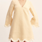 A woman wears the POSSE Essie Kaftan, a light beige long-sleeve vacation dress with a deep V-neckline and scalloped hem and sleeve edges trimmed with white fringe.