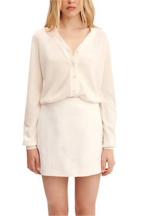 A woman stands against a plain background wearing the POSSE Alice Skirt, a cream linen mini with an A-line silhouette, paired with a matching long-sleeve button-front blouse.