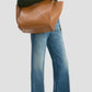 A person in a green ribbed sweater and wide-leg blue jeans carries the Victoria Beckham Small Victoria Tote in tan leather over their shoulder.
