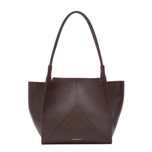 The Victoria Tote by Victoria Beckham is a dark brown Italian-crafted bag with two handles, a structured geometric design, and a luxurious suede-lined interior.