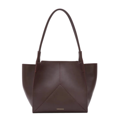 The Victoria Tote by Victoria Beckham is a dark brown Italian-crafted bag with two handles, a structured geometric design, and a luxurious suede-lined interior.