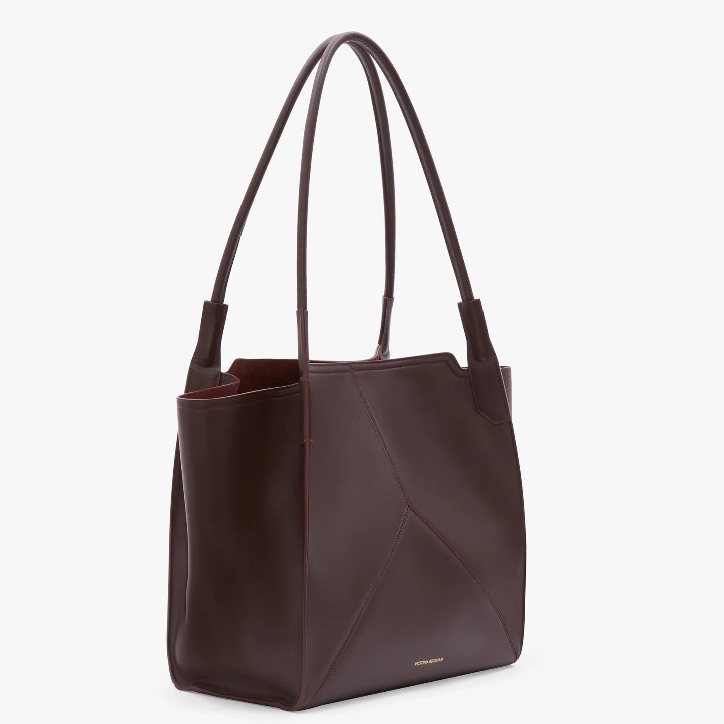 The Victoria Beckham Victoria Tote, in dark brown leather with double shoulder straps and minimal stitching, features a luxe suede-lined interior and stands upright on a white background.