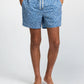 A person wearing Onia Charles 5" Swim Trunk in blue with a white floral pattern, standing barefoot against a plain background.