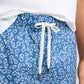 A person wearing Onia Charles 5" Swim Trunk in a blue floral pattern with a white drawstring and a white top, shown from the waist down.