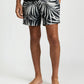 A person stands barefoot in Onia's Charles 5" Swim Trunk, featuring a bold palm leaf pattern and classic tailoring, paired with a black shirt. The photo is cropped above the waist.