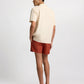 A man faces away, wearing the Onia Linen Pintuck Camp Shirt with pintuck pleats, paired with rust shorts and brown loafers against a plain light background.