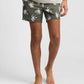 A person stands barefoot against a plain background wearing Onia’s Charles 5" Swim Trunk in olive green with a white palm tree print, made from quick-dry fabric.