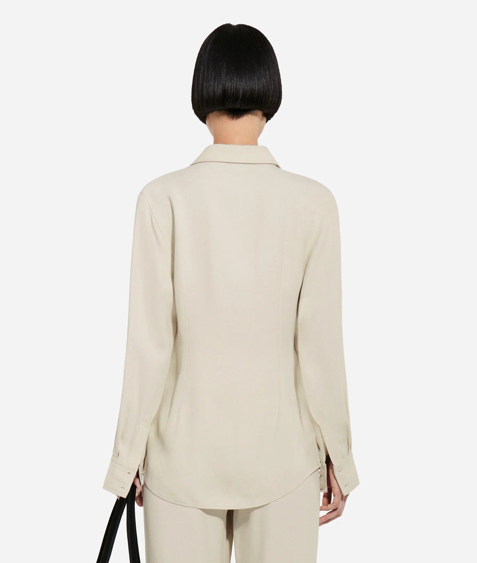 A person with short, straight black hair wears the CO Fitted Collared Shirt in light beige, paired with matching pants. They are standing with their back to the camera against a plain background.