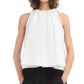 Woman wears the CO Gathered Tunic Shirt, a sleeveless cotton poplin top in a loose-fitting halter style, paired with black pants. Shown from the waist up with hands in pockets.