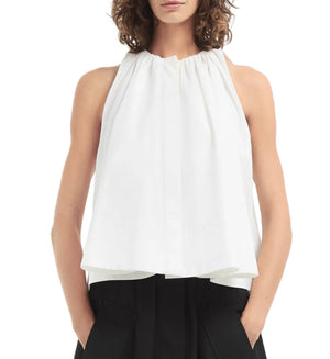 Woman wears the CO Gathered Tunic Shirt, a sleeveless cotton poplin top in a loose-fitting halter style, paired with black pants. Shown from the waist up with hands in pockets.