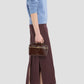 Woman in profile wears a light blue sweater, dark midi skirt with side slits, black heeled sandals, and carries the Victoria Beckham Vanity Croc Crossbody handbag.