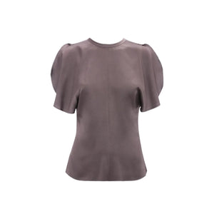 The Bela Top by Victoria Beckham is a short-sleeved, mauve blouse with puffed shoulders and a round neckline, made from grey crepe back satin and shown on a white background.