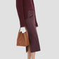 A person in a burgundy ribbed sweater, dark purple midi skirt, red open-toe heels, and carrying the Victoria Beckham Victoria Bucket bag in Dark Tan nappa leather completes this modern look.