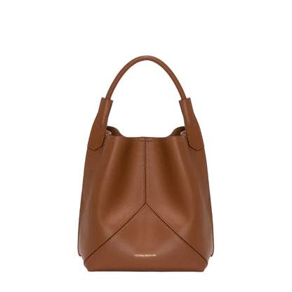 The Victoria Bucket by Victoria Beckham features a modern look in dark tan nappa leather, with a single handle, visible seam details, and the brand’s logo on the lower front.