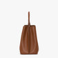 Side view of the Victoria Beckham Victoria Bucket bag in dark tan nappa leather, with a structured shape and single top handle, shown on a plain white background.
