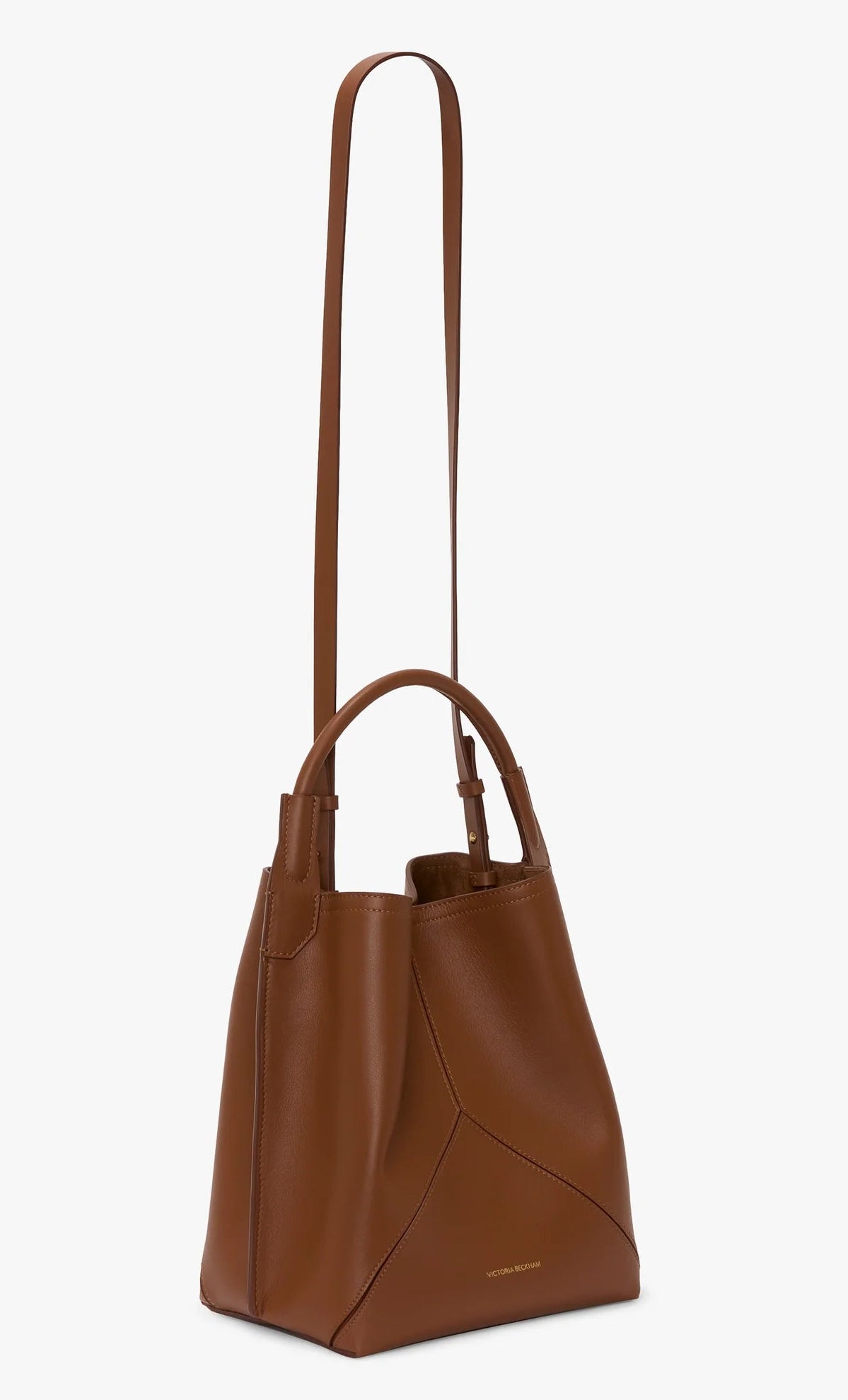 The Victoria Beckham Victoria Bucket in dark tan nappa leather features dual handles, a long shoulder strap, clean lines, and minimal gold branding at the base for a modern look.