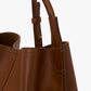 Close-up of the Victoria Beckham Victoria Bucket bag in dark tan nappa leather, showcasing its handle and precise stitching details against a plain white background for a modern aesthetic.