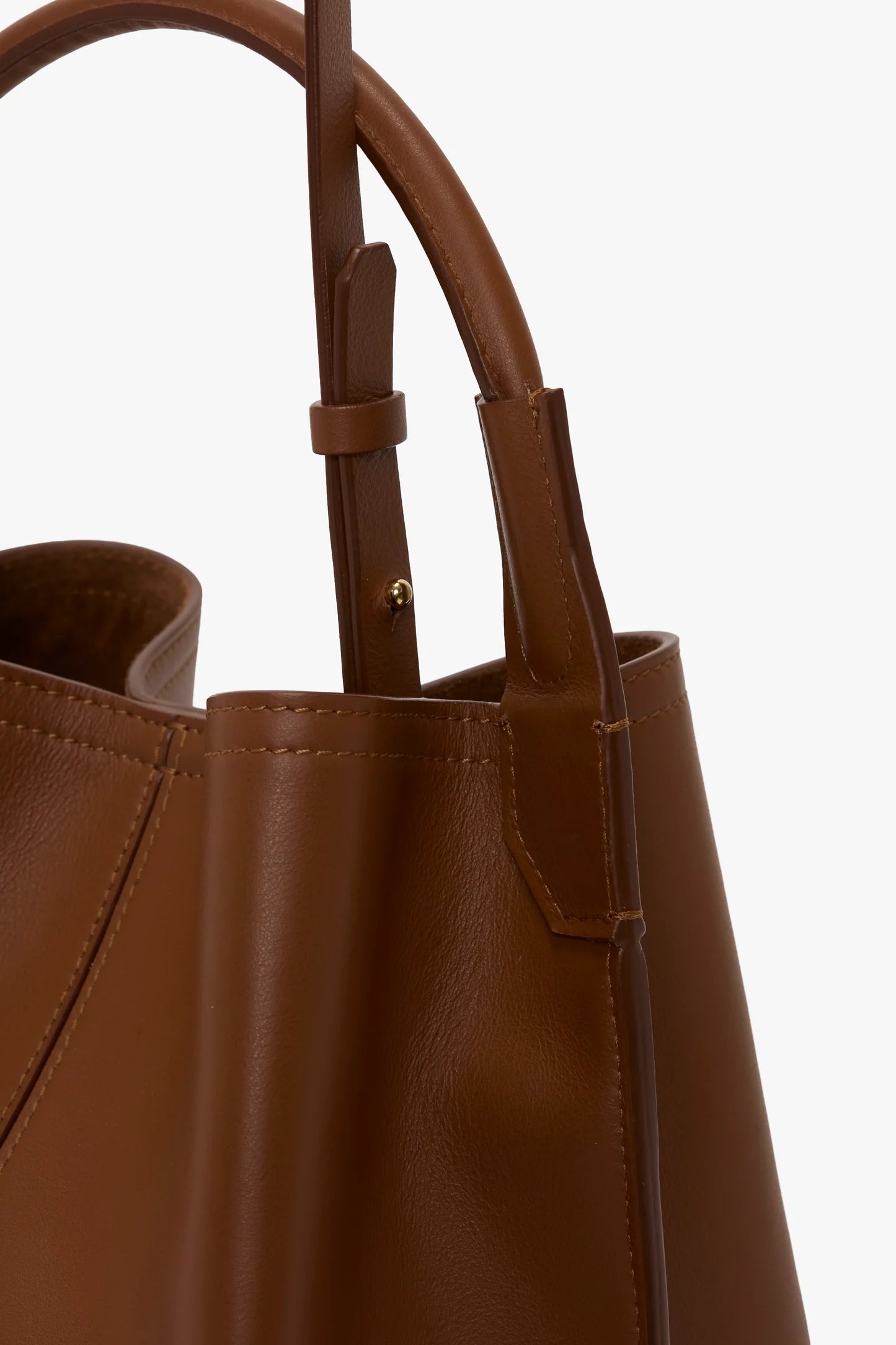 Close-up of the Victoria Beckham Victoria Bucket bag in dark tan nappa leather, showcasing its handle and precise stitching details against a plain white background for a modern aesthetic.