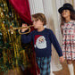 A boy wearing a Pink Chicken Boys’ Oliver Sweater with a jolly Santa graphic plays a gold trumpet next to a girl in a Santa-print dress and a black hat.