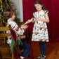 A girl in a Pink Chicken Girls’ Jennifer holiday twirl dress hands a program to a boy in a matching button-down shirt.