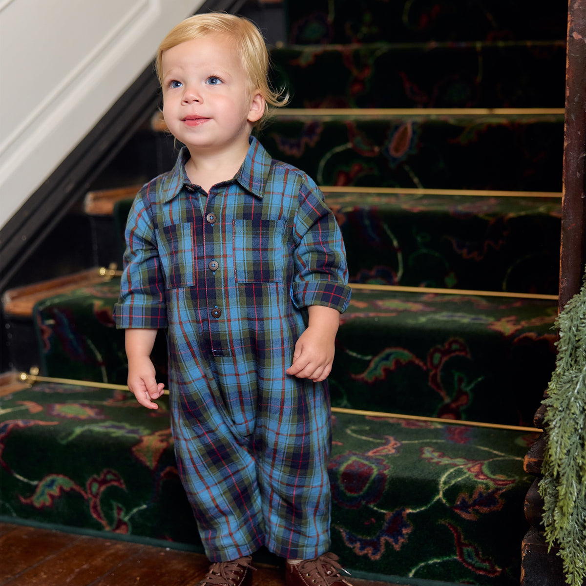 A toddler wearing a blue and green tartan Baby Boys’ Easton Jumper standing on a staircase.