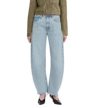 Model wears The Bubble Crop high-rise wide-leg jeans by Frame in light blue, paired with an olive green jacket and black pointed-toe shoes, standing against a white background.