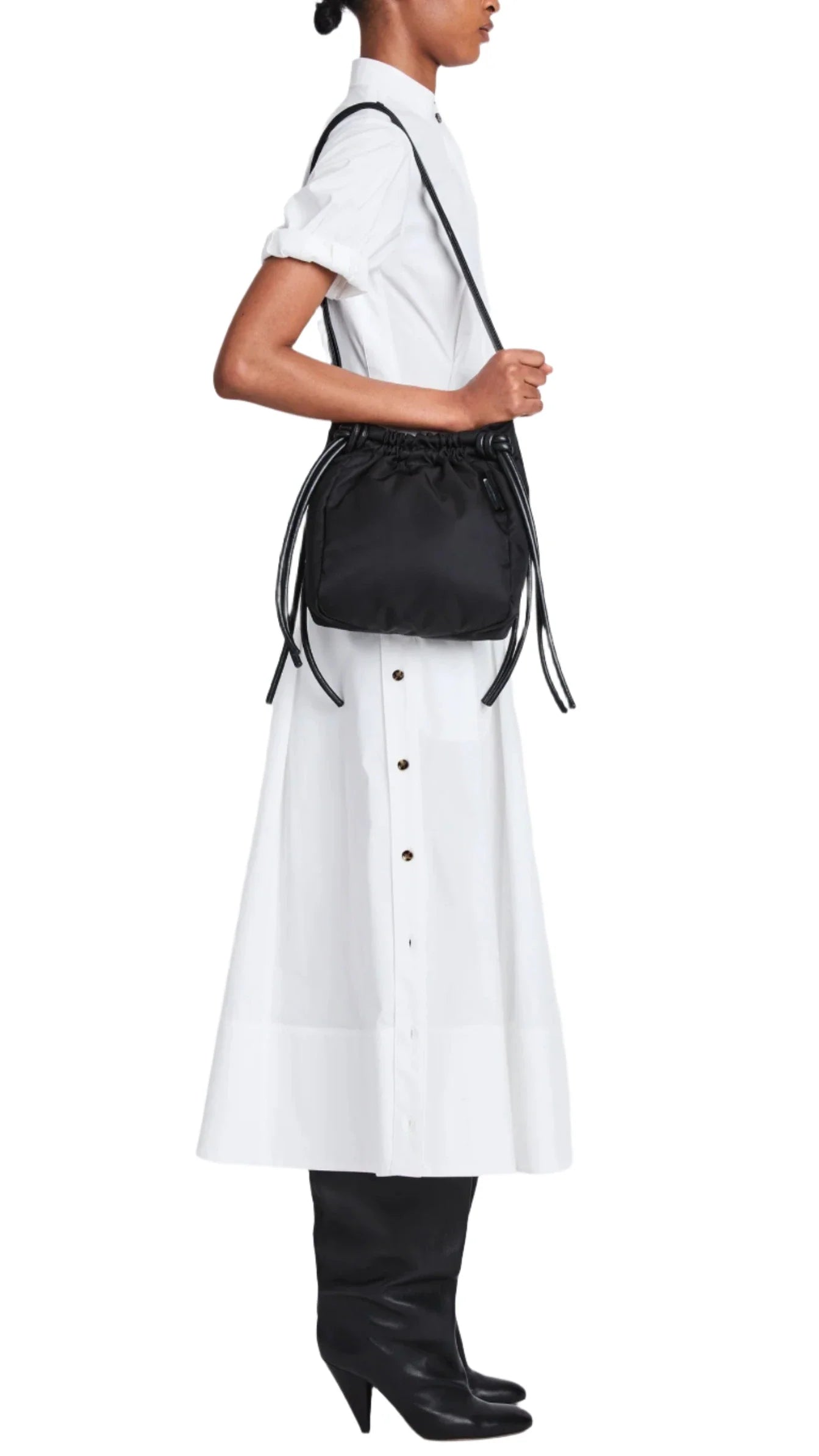 Person wearing a white dress with side buttons and black boots, carrying the Proenza Schouler Drawstring Nylon Tote.