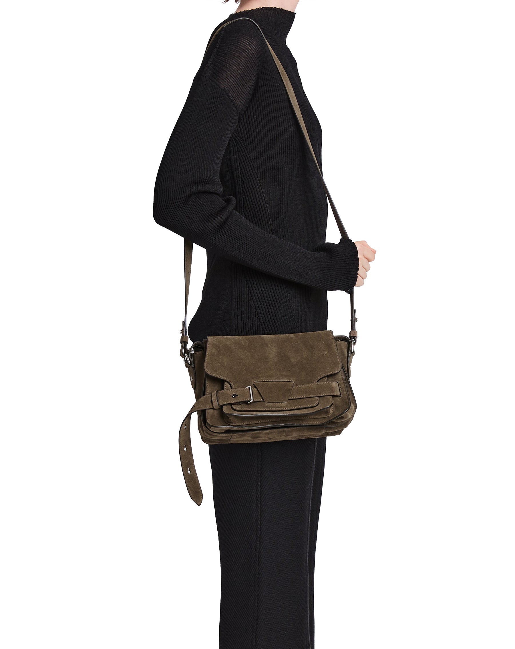 A person standing sideways wearing a black outfit with a brown suede Proenza Schouler Suede Beacon Saddle Bag on their shoulder.