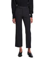A person is wearing the Proenza Schouler Marlene Tropical Wool Pant in black, featuring a high-rise and cropped length, styled with a black top and black heeled shoes, standing facing forward against a plain white background.