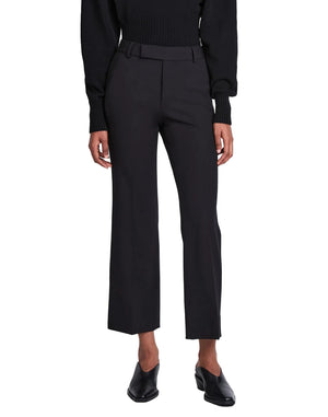A person is wearing the Proenza Schouler Marlene Tropical Wool Pant in black, featuring a high-rise and cropped length, styled with a black top and black heeled shoes, standing facing forward against a plain white background.