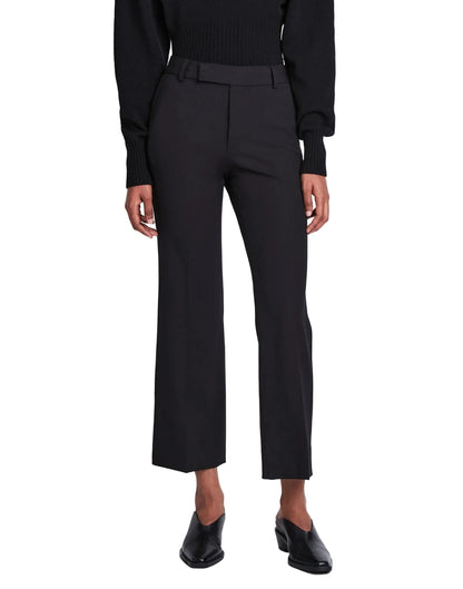 A person is wearing the Proenza Schouler Marlene Tropical Wool Pant in black, featuring a high-rise and cropped length, styled with a black top and black heeled shoes, standing facing forward against a plain white background.
