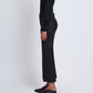 Standing sideways against a plain white background, the person wears the Proenza Schouler Marlene Tropical Wool Pant in black. Their head and upper body are out of frame, and they style the pants with a black cropped sweater and black slip-on shoes.