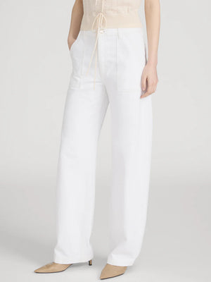 Wearing Frame’s The Bow Cargo high-rise barrel jeans with front cargo pockets, a light sleeveless top, and beige pointed-toe heels, a person stands against a plain background for a modern utilitarian look.