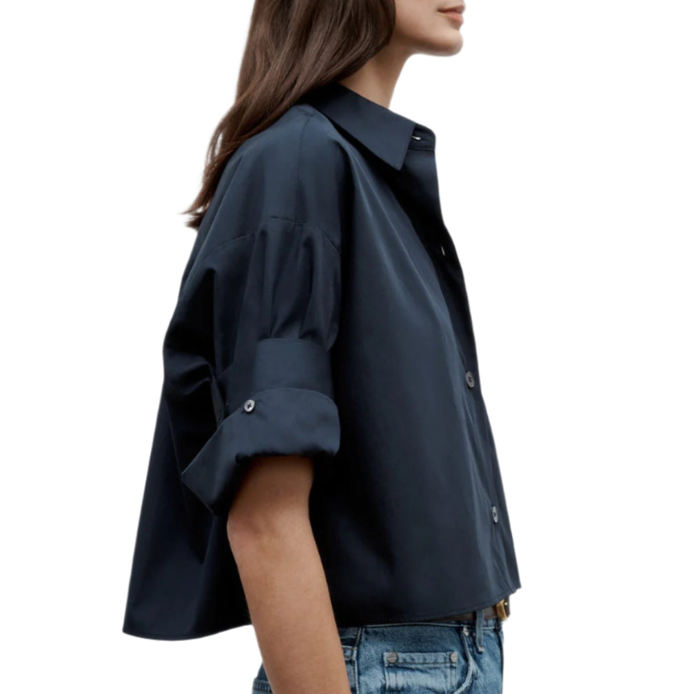 A woman wears the TWP Next Ex Shirt, a vintage washed poplin short-sleeve button-up with rolled cuffs, paired with light blue jeans, shown from the side against a white background.