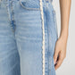 Close-up of a person wearing Frame’s The Crochet Bow Crop jeans in light blue denim, featuring scalloped white crochet trim along the side seam; their hand rests at their side.