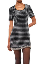 A person dressed in the elegant Simkhai Vivalie Mini Dress, showcasing a chic black and white checkered pattern, short sleeves, and a rounded neckline. This relaxed fit provides a flattering silhouette that gracefully balances elegance with comfort.