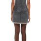 Back view of a person in the Simkhai Vivalie Mini Dress, featuring a black and white checkered pattern with short sleeves, paired with black tights, highlighting an elegant silhouette against a white background.