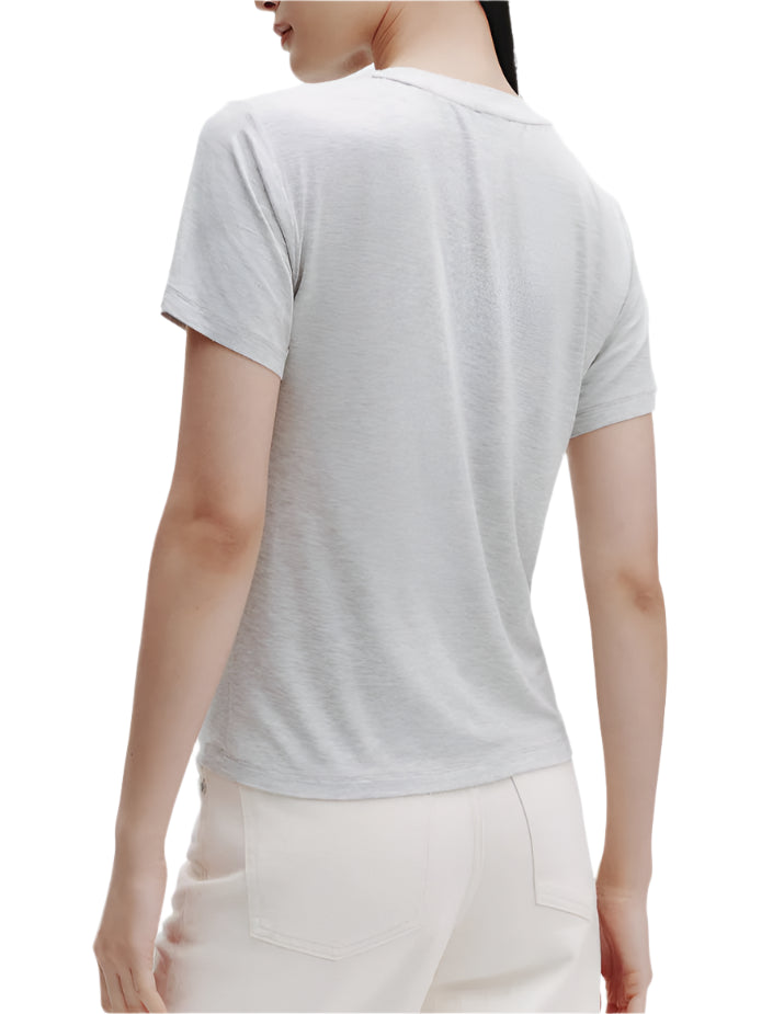 Model wears the TWP His Tee in light gray ultra-soft cotton and white pleated pants, shown from the back against a plain background.