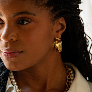 A woman with braided hair wears Juliska Capucine De Wulf Berry Classic Medium Hoop Earrings, a gold chain necklace, and a pearl necklace, looking slightly to the left.