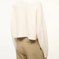 A person shown from the back wearing the Staud Cropped Hampton Cashmere Sweater in white with long sleeves, paired with high-waisted beige trousers.