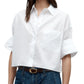 Wearing the TWP Next Ex Shirt, a vintage washed white poplin button-up with rolled sleeves, tucked into high-waisted blue jeans and styled with a brown belt.