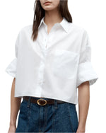 Wearing the TWP Next Ex Shirt, a vintage washed white poplin button-up with rolled sleeves, tucked into high-waisted blue jeans and styled with a brown belt.