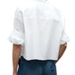 A person wearing the TWP Next Ex Shirt, a vintage washed white poplin button-up with rolled sleeves, paired with blue jeans, shown from the back.