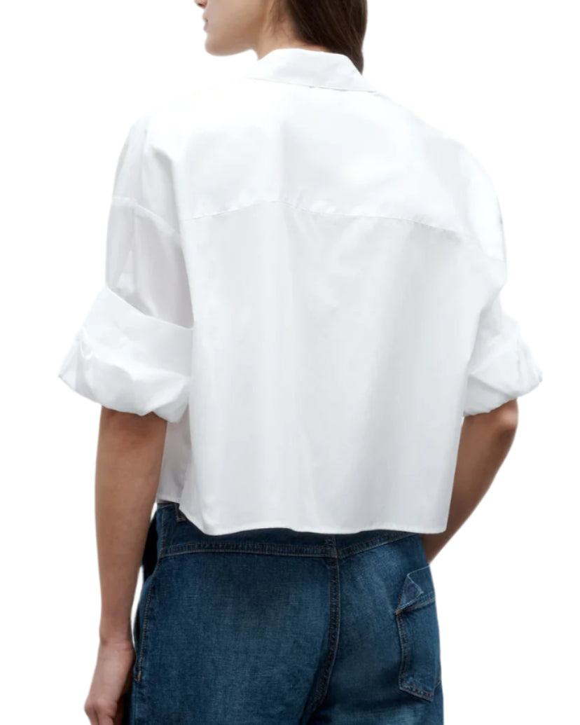 A person wearing the TWP Next Ex Shirt, a vintage washed white poplin button-up with rolled sleeves, paired with blue jeans, shown from the back.