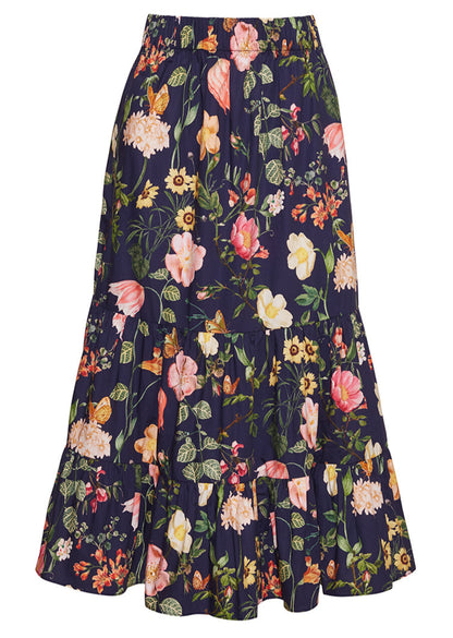 The Chase Skirt by Cara Cara is a dark blue cotton poplin midi skirt with colorful floral and leaf prints, an elastic waistband, and tiered design.