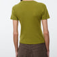 A person stands facing away against a plain light background, wearing the Staud Easy Cashmere Tee—a short-sleeved, olive green cashmere top with a crew neckline—paired with brown pants.